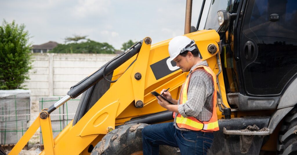 construction man assessing side boom mower maintenance with clip board